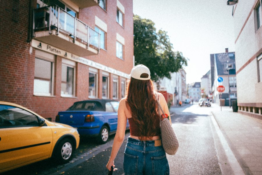 Woman in a white cap walking down a residential street, seen from behind