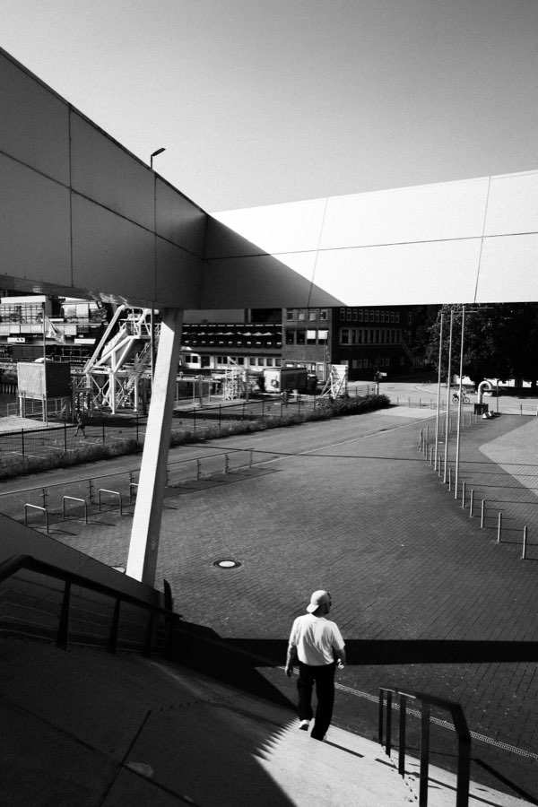 Black and white photo of a man walking past a modern glass building