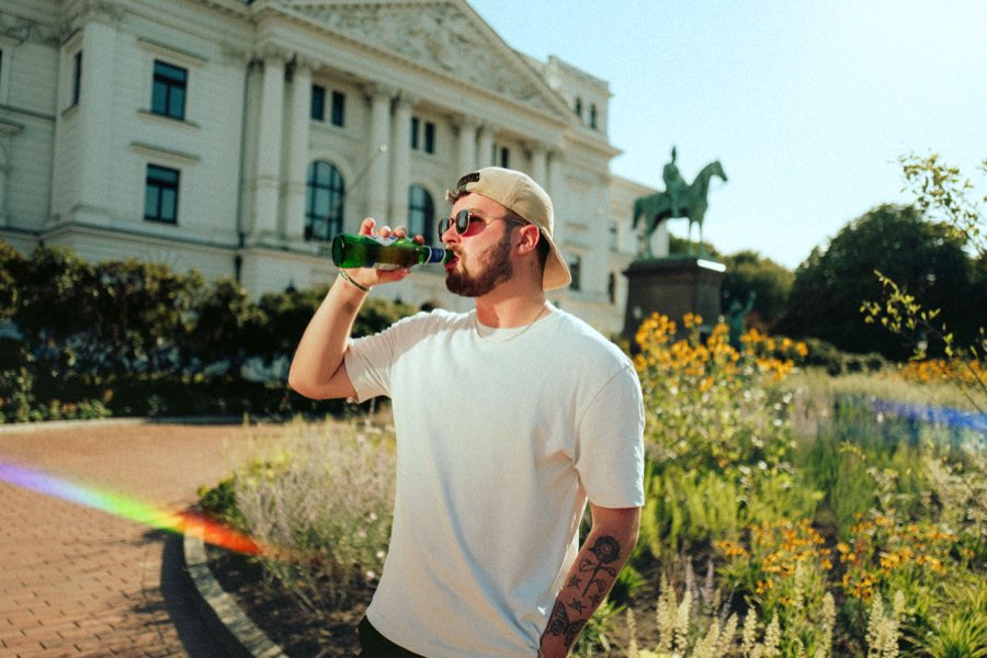 Man in a cap drinking from a bottle in front of a palace garden