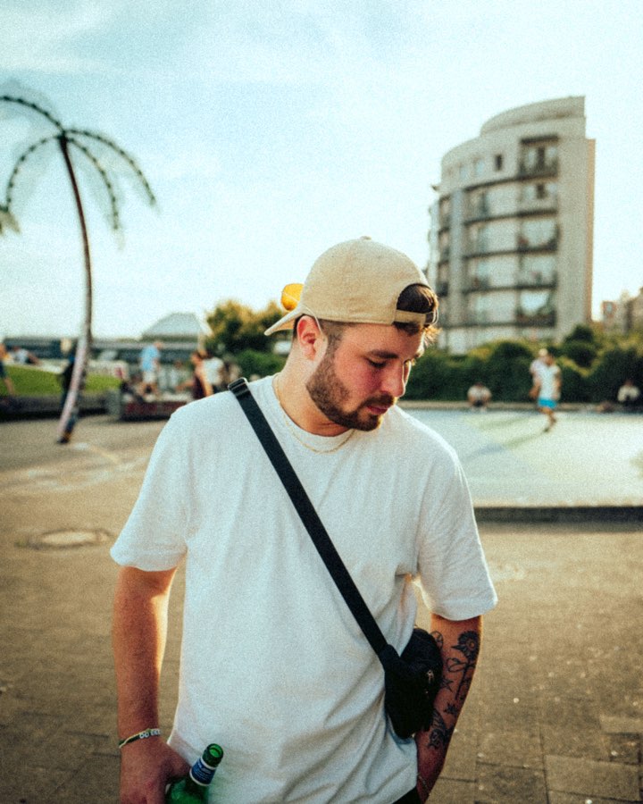 Man in a cap and white T-shirt standing by palm trees on a sunny square