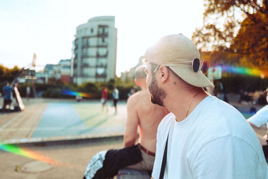 Man in a cap sitting in the sun with city buildings behind him