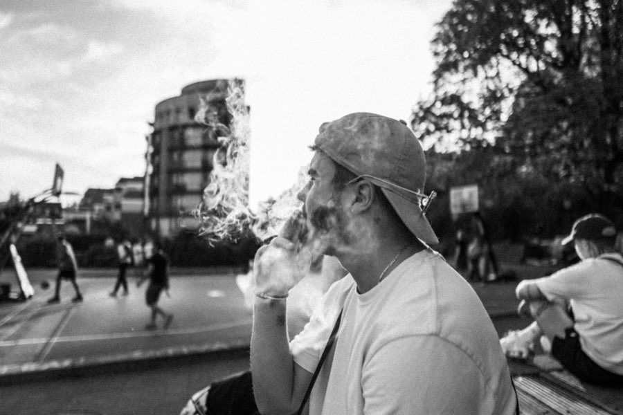 Black and white photo of a man in a cap smoking on a busy street