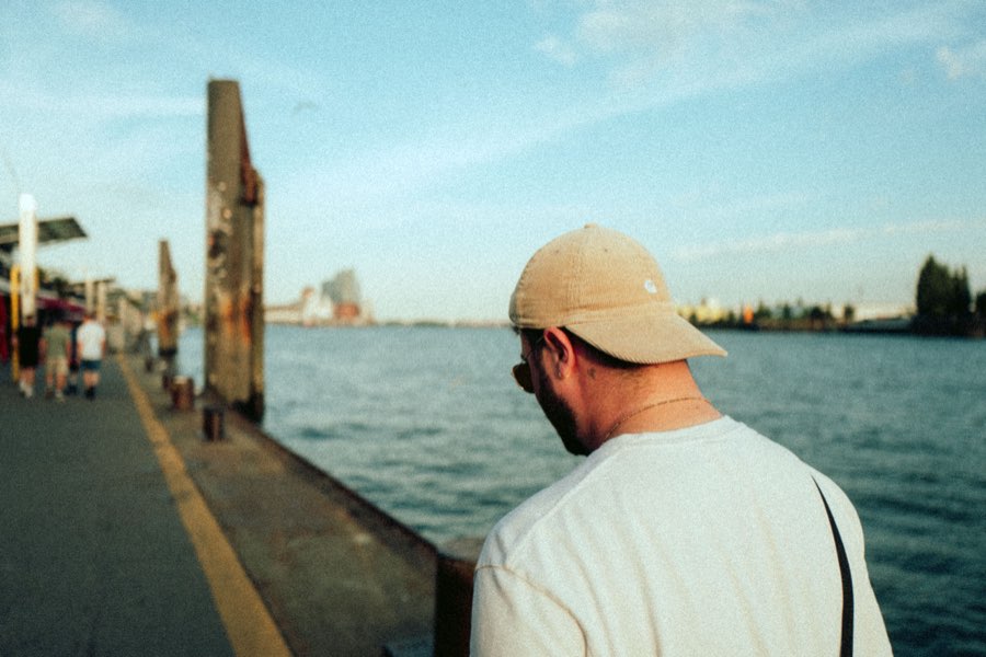 Man in a cap looking out over a river from a pier, seen from behind
