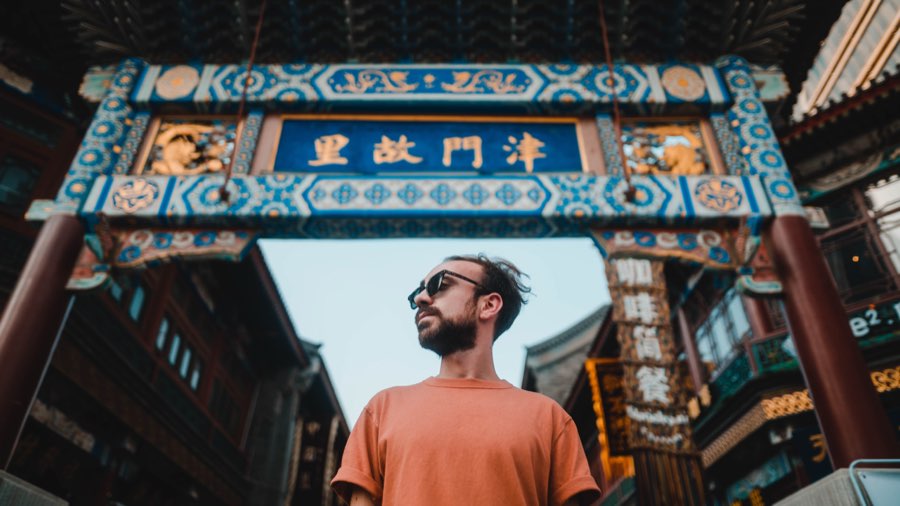 Man in an orange T-shirt and sunglasses beneath an ornate Chinese gate