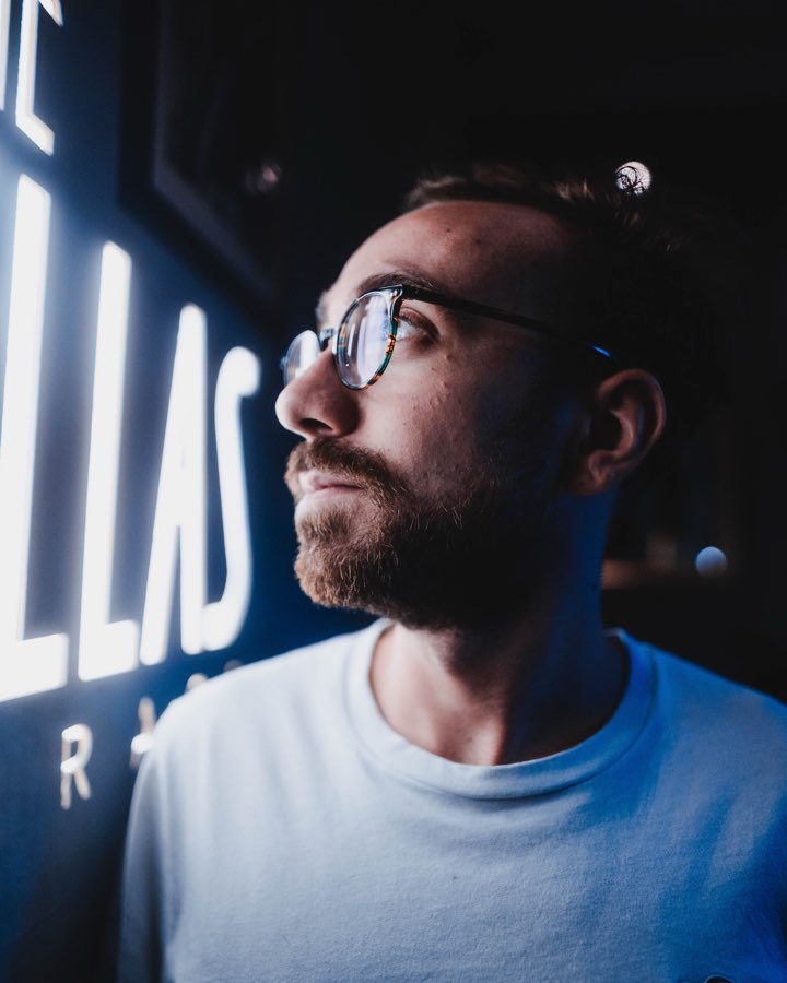Man with glasses lit by a neon sign at night