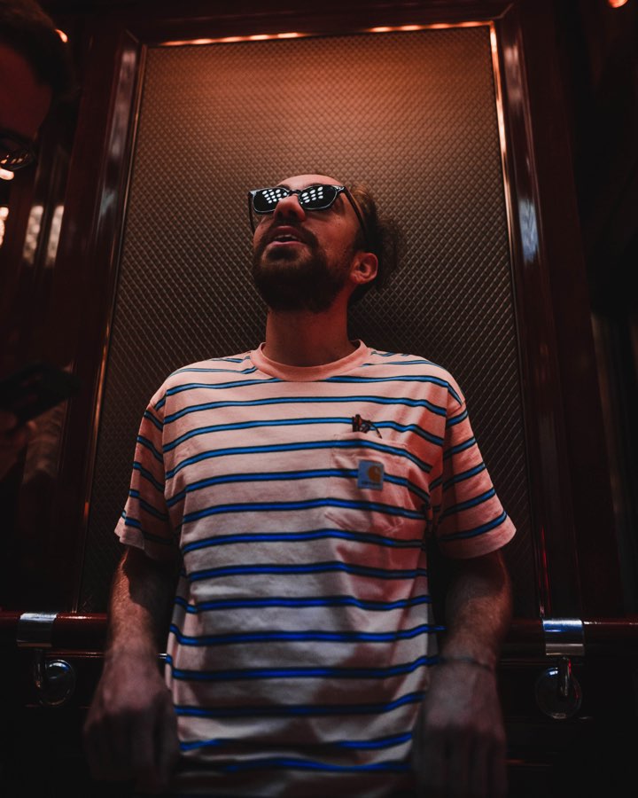 Man in sunglasses and a striped shirt standing in a dark lift
