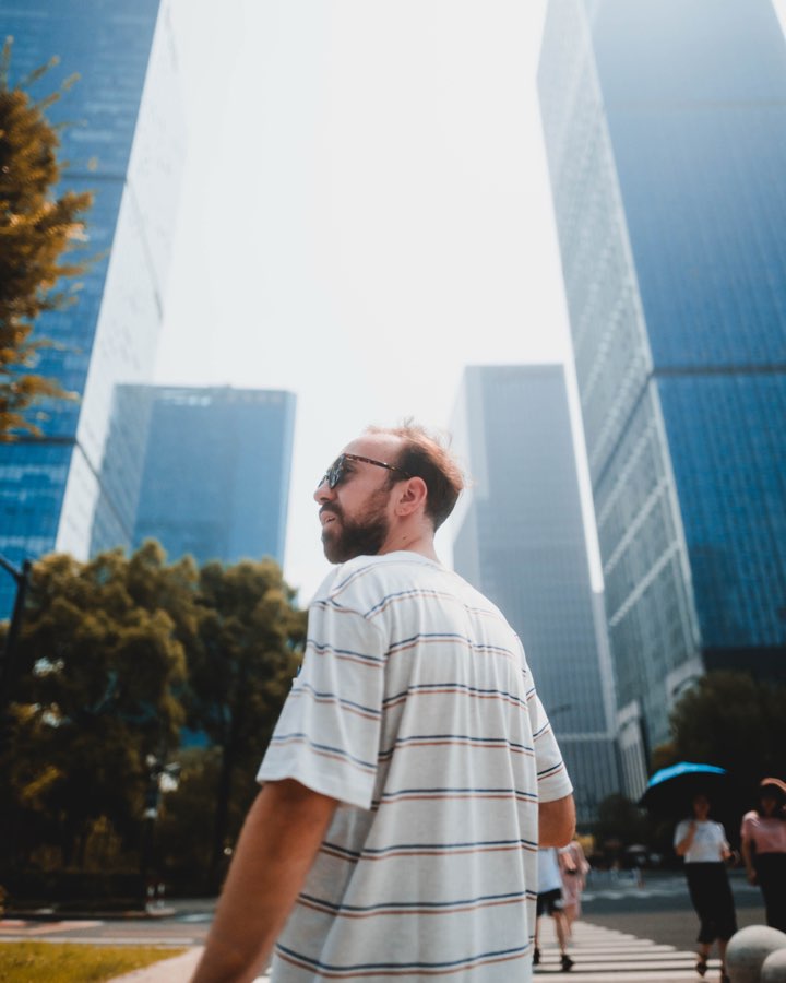 Man in a striped shirt looking up at tall glass skyscrapers