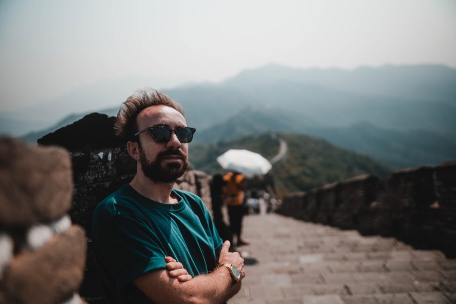 Man in sunglasses with arms crossed on an ancient stone wall in the mountains