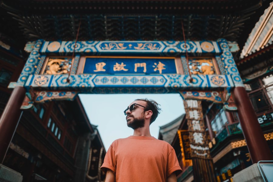 Man in an orange T-shirt looking up beneath an ornate gate