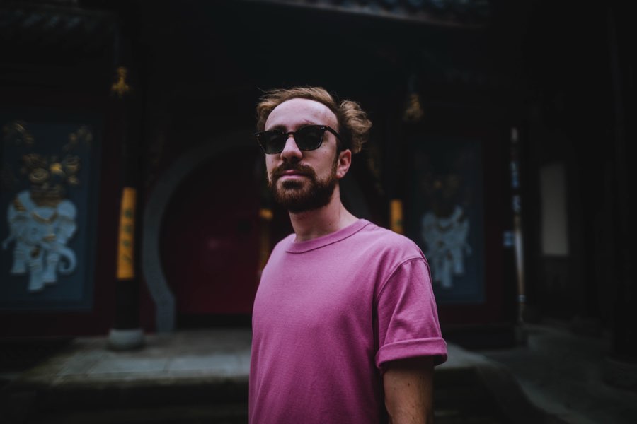 Man in sunglasses and a pink T-shirt in front of a dark temple