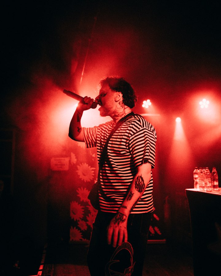 Performer in a striped shirt singing into a microphone in red stage light