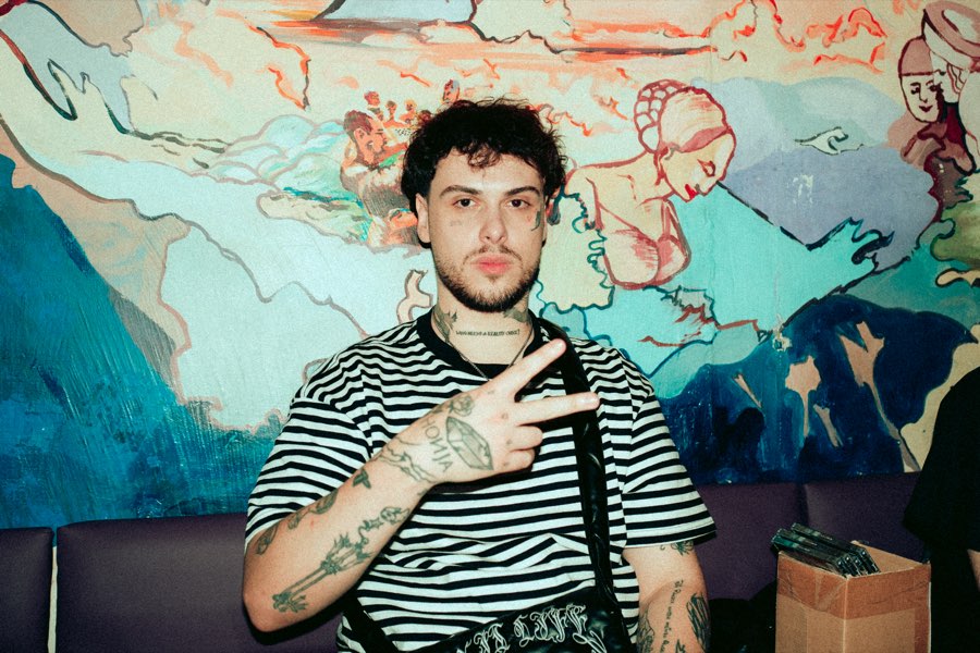 Smiling man in a striped shirt making a peace sign in front of a colourful mural