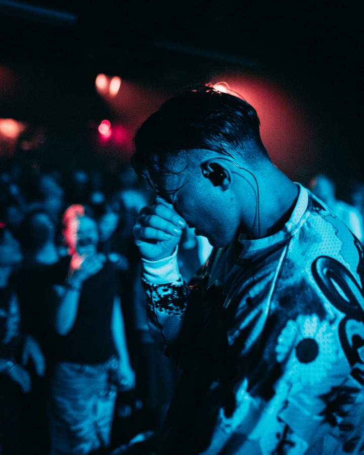 Performer covering his face with his hand in blue and red club light