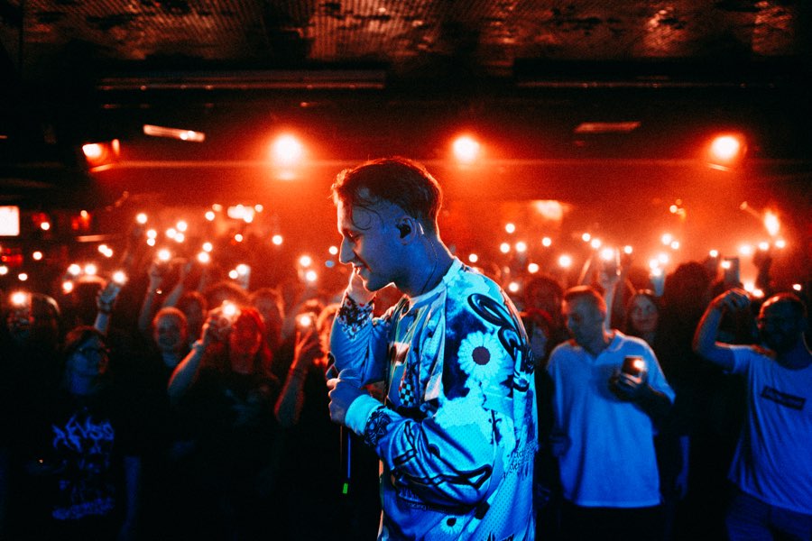 Performer in a printed jacket in front of a crowd holding up phone lights