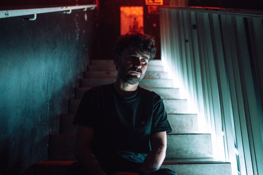 Man in glasses sitting on stairs in dim teal light