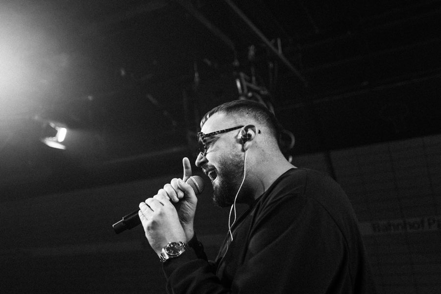 Black and white photo of a performer in glasses rapping into a microphone