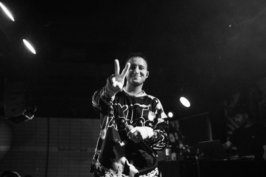 Black and white photo of a smiling performer making a peace sign on stage