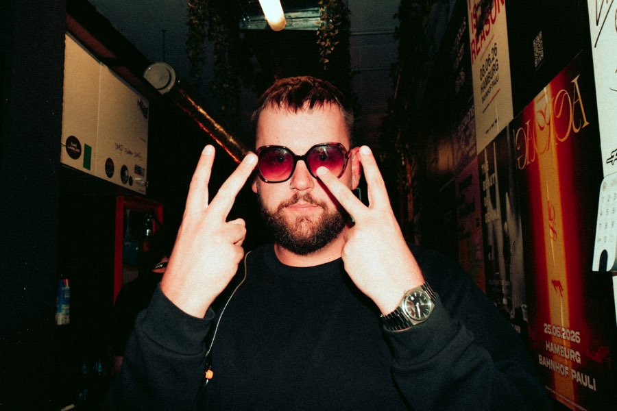 Man in red sunglasses making horns gestures in a backstage corridor