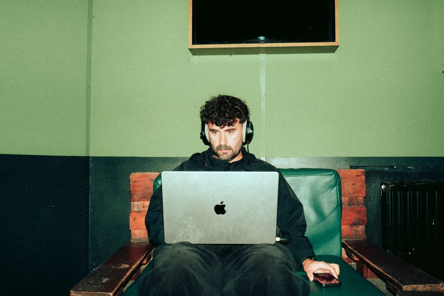 Man with headphones working on a laptop in a green backstage room