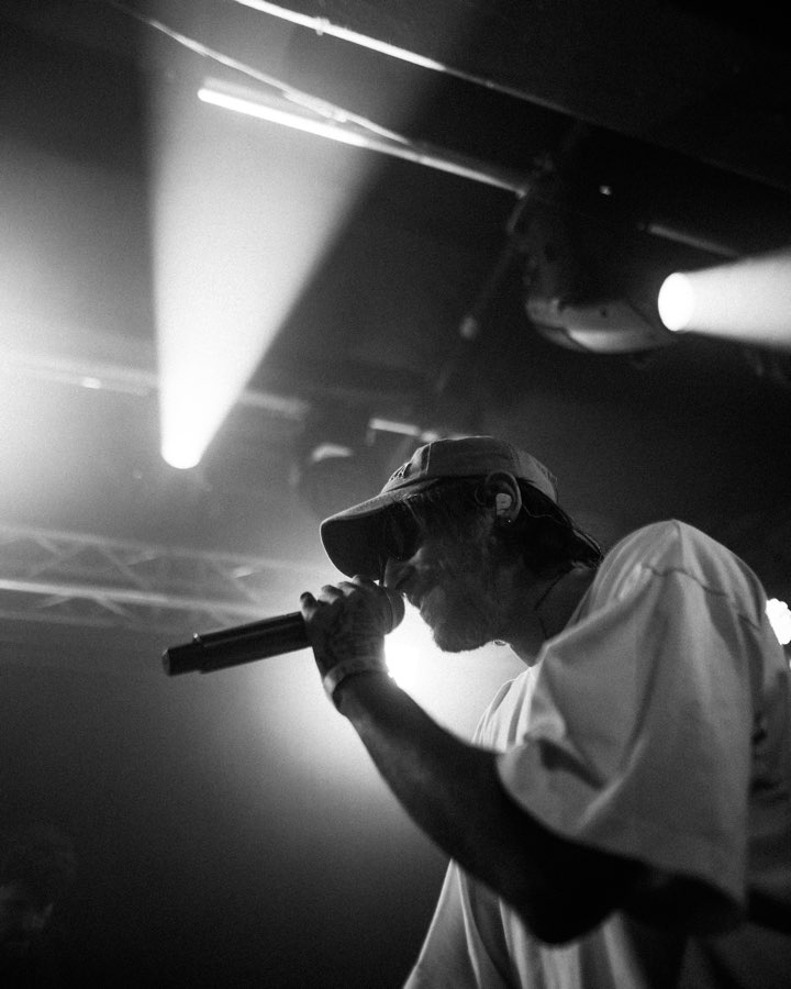 Black and white photo of a performer in a cap rapping under bright spotlights