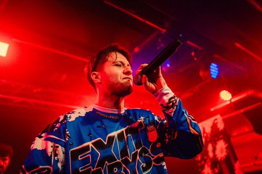 Performer in an Exit Abyss jersey holding a microphone in red and blue light