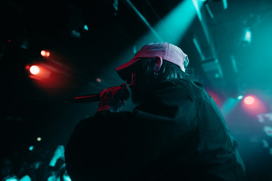 Performer in a cap seen from behind under teal and red stage lights
