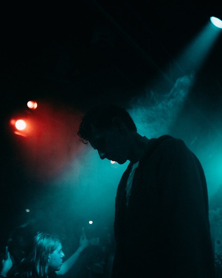 Silhouette of a performer with bowed head in teal and red stage light