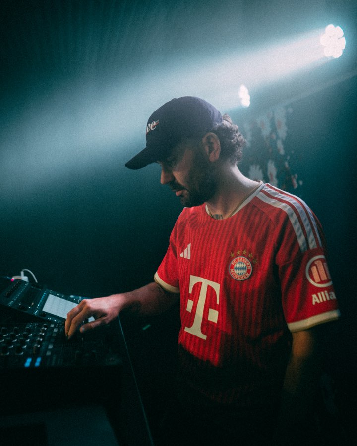 DJ in a cap and red football shirt at the decks under a spotlight