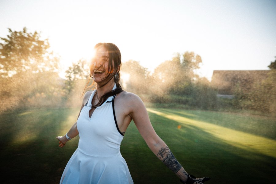 Laughing woman in a white dress in sunlit mist on a golf course