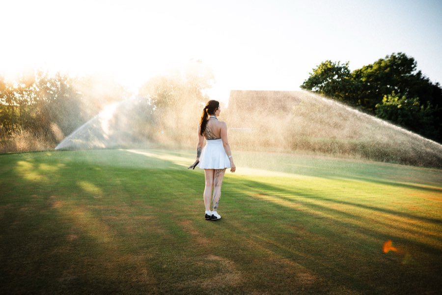 Woman in a white dress standing in sprinkler spray on a golf course