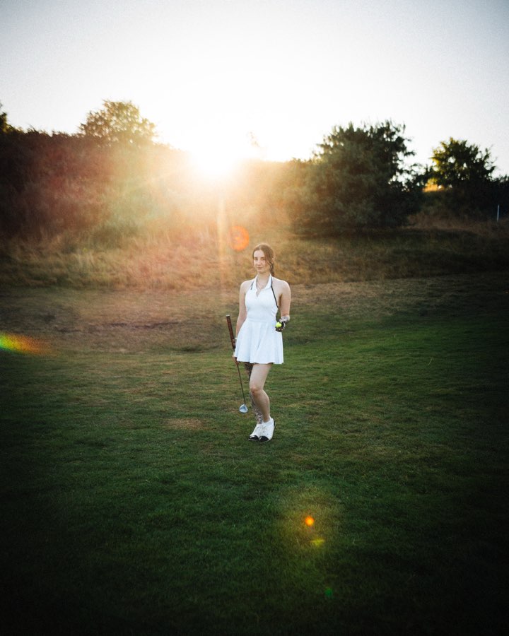 Woman in a white dress walking across a meadow towards the setting sun