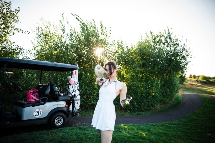 Woman in a white dress holding a golf club beside a golf cart