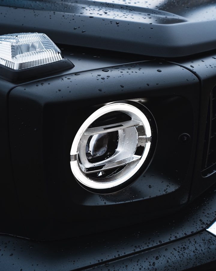 Close-up of the round LED headlight of a Mercedes G 63 with raindrops