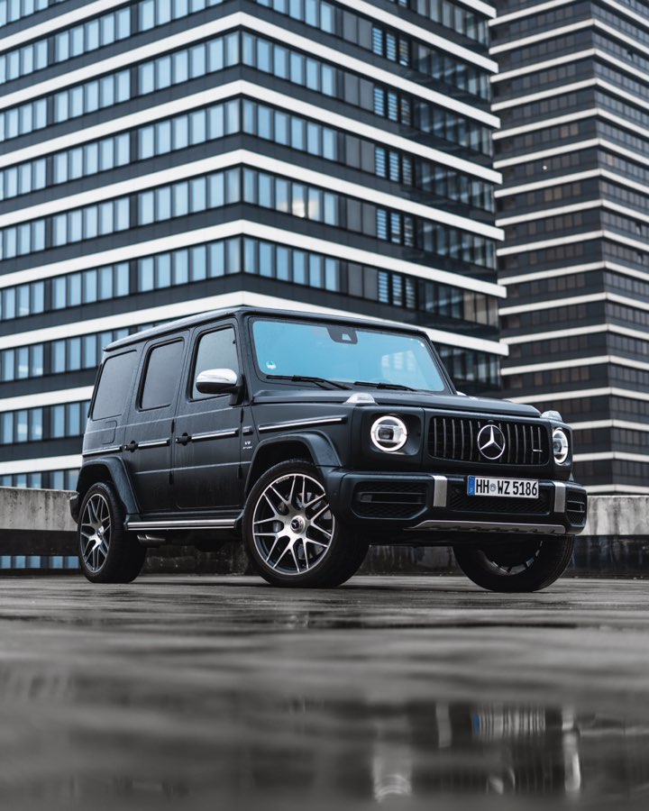 Black Mercedes G 63 on a wet rooftop car park in front of an office tower