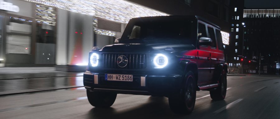 Black Mercedes G 63 with glowing headlights driving through a city street at night