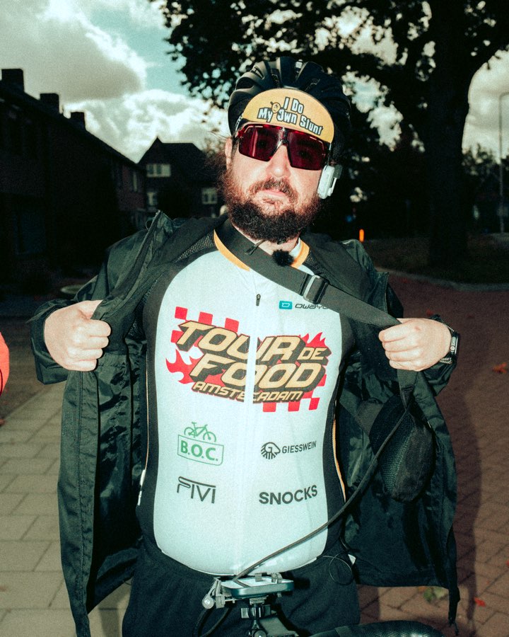 Bearded man in red sunglasses opening his jacket to show a Tour de Food jersey