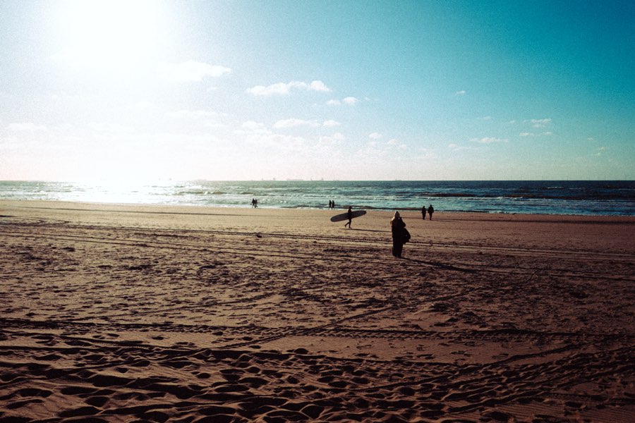 People walking along a wide sandy beach in low sunlight