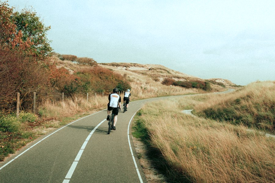 Two cyclists riding along a path through autumn dunes