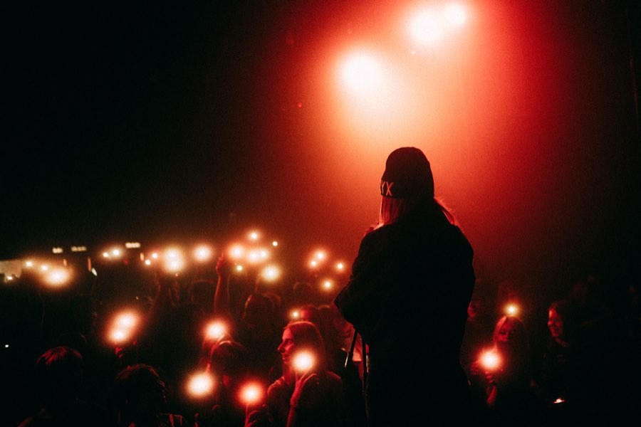 Singer in silhouette in front of a crowd holding up phone lights, red stage light