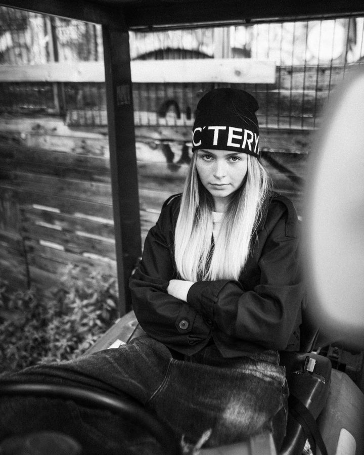 Woman in a beanie and black jacket in front of a graffiti wall