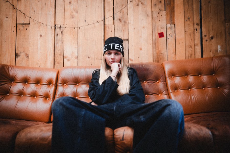 Woman in a beanie sitting on a brown leather sofa against a wooden wall